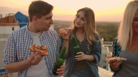 Una-Pareja-Amorosa-En-El-Techo-Bebe-Cerveza-De-Botellas-Verdes-Y-Come-Pizza.-La-Chica-Mira-Tímidamente-Y-Con-Ternura-A-Su-Novio.